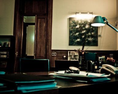 En una oficina con poca luz, que recuerda al Escape Room Misterio del Profesor Waichosky en Zaragoza 🕵️‍♂️, el escritorio de madera de Waichosky está abarrotado de papeles. Una lámpara de tenue luz proyecta sombras sobre un cuadro de Zaragoza, realzando la atmósfera intrigante. - ForTwo - Planes para parejas
