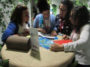 Cuatro mujeres conversaban en una mesa con mapas y artefactos, en una sala adornada con vegetación. El ambiente evocaba la famosa aventura de Escape Room Misterio del Profesor Waichosky en Zaragoza. - ForTwo - Planes para parejas