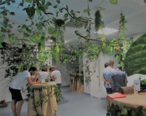 La sala rezuma el encanto encantador de Zaragoza, adornada con plantas colgantes y vegetación, mientras la gente se reúne alrededor de mesas cubiertas con telas marrones para experimentar la cautivadora 🕵️‍♂️ Escape Room Misterio del Profesor Waichosky en Zaragoza 🔐🧩. - ForTwo - Planes para parejas