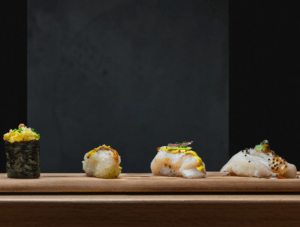 Akiro Barcelona: Un Viaje Gastronómico a Japón para Dos" presenta una variedad de sushi gourmet artísticamente dispuesto sobre una tabla de madera sobre un fondo oscuro, ofreciendo un auténtico viaje culinario japonés. - ForTwo - Planes para parejas