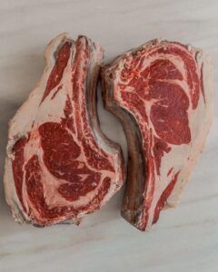 Dos filetes de chuletón crudos y marmolados reposan sobre una superficie de mármol claro, evocando las exquisitas ofertas de El Paraíso de la Carne en Zaragoza. - ForTwo - Planes para parejas