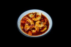 Experimente los ricos sabores de una cena japonesa con la Cena japonesa en Más que Sushi: suculentos camarones en salsa roja con vegetales vibrantes, sobre un elegante fondo negro para una delicia culinaria que va más allá del sushi. - ForTwo - Planes para parejas