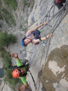 Sonrientes escaladores, un hombre y una mujer, abordan el acantilado rocoso de la Cascada del Sorrosal durante su "Curso de Vía Ferrata en la Cascada del Sorrosal", asegurados con cuerdas y cascos para una aventura llena de emoción y recuerdos inolvidables. - ForTwo - Planes para parejas