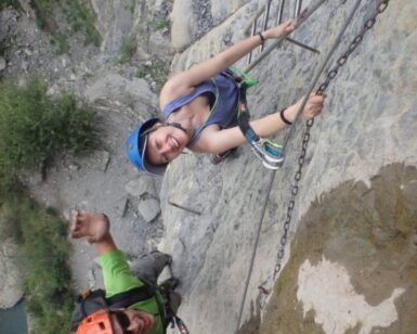 Sonrientes escaladores, un hombre y una mujer, abordan el acantilado rocoso de la Cascada del Sorrosal durante su "Curso de Vía Ferrata en la Cascada del Sorrosal", asegurados con cuerdas y cascos para una aventura llena de emoción y recuerdos inolvidables. - ForTwo - Planes para parejas