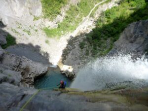 Una persona desciende hábilmente en rápel por un acantilado empinado junto a la Cascada del Sorrosal, hasta llegar a la piscina rocosa de abajo, una escena emocionante que recuerda al Curso de Vía Ferrata en la Cascada del Sorrosal. - ForTwo - Planes para parejas