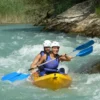 Dos individuos con casco navegan por el turbulento Río Gállego en una canoa amarilla con remos azules, parte de la experiencia Descenso en Canoa por el Río Gállego. - ForTwo - Planes para parejas
