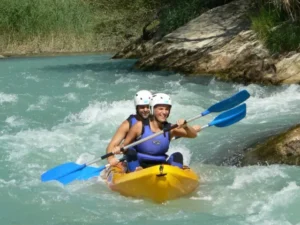 Dos individuos con casco navegan por el turbulento Río Gállego en una canoa amarilla con remos azules, parte de la experiencia Descenso en Canoa por el Río Gállego. - ForTwo - Planes para parejas