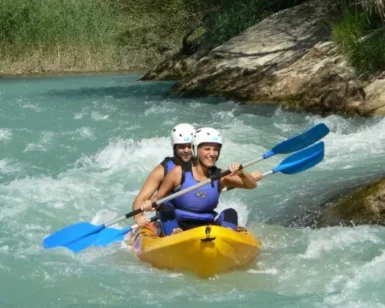 Dos individuos con casco navegan por el turbulento Río Gállego en una canoa amarilla con remos azules, parte de la experiencia Descenso en Canoa por el Río Gállego. - ForTwo - Planes para parejas