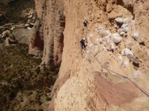 Los escaladores que usan cuerdas navegan por la escarpada y rocosa pared del acantilado de Calcena con un pintoresco pueblo visible debajo, mientras disfrutan de la "Escalada Guiada en Calcena". - ForTwo - Planes para parejas