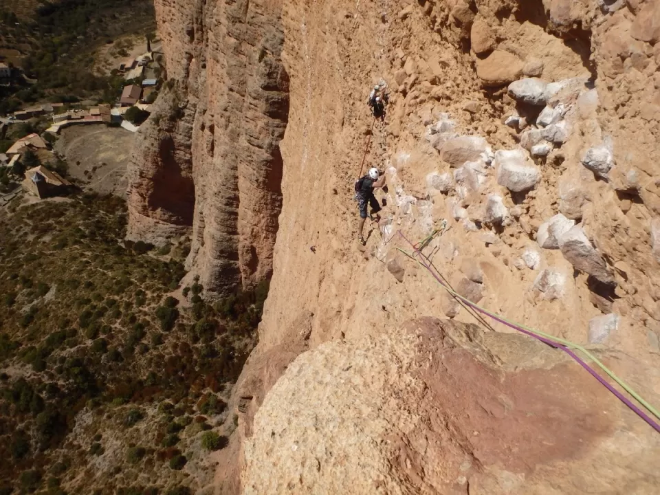 Los escaladores que usan cuerdas navegan por la escarpada y rocosa pared del acantilado de Calcena con un pintoresco pueblo visible debajo, mientras disfrutan de la "Escalada Guiada en Calcena". - ForTwo - Planes para parejas