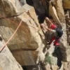 Un escalador con equipo rojo asciende un acantilado empinado en Calcena, atado de forma segura y aceptando el desafío de la Escalada Guiada en Calcena bajo el cielo soleado. - ForTwo - Planes para parejas