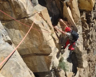 Un escalador con equipo rojo asciende un acantilado empinado en Calcena, atado de forma segura y aceptando el desafío de la Escalada Guiada en Calcena bajo el cielo soleado. - ForTwo - Planes para parejas