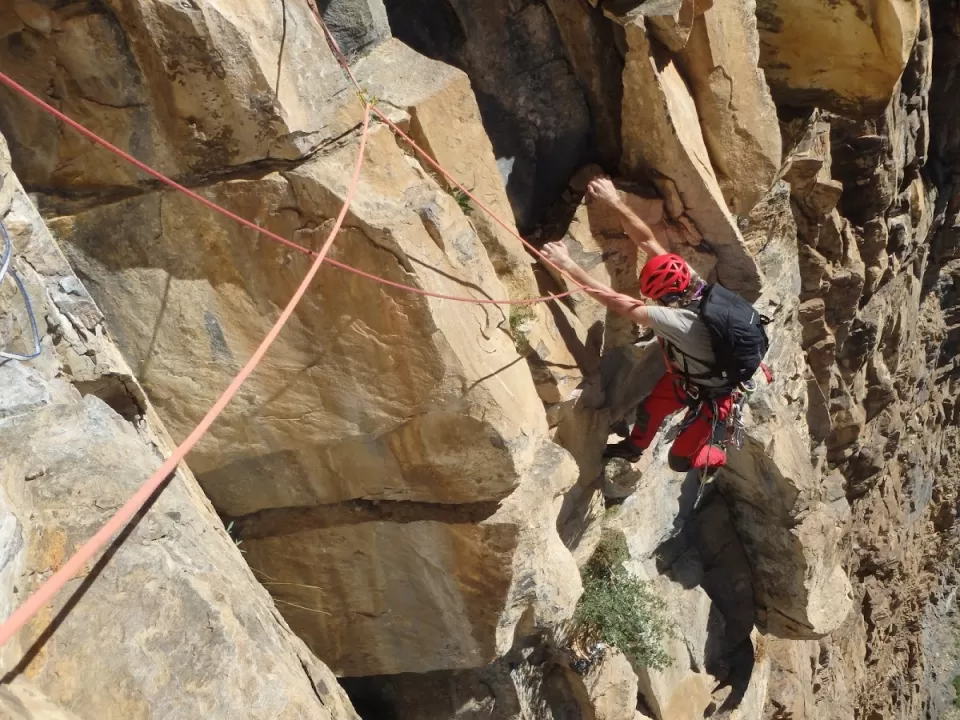 Un escalador con equipo rojo asciende un acantilado empinado en Calcena, atado de forma segura y aceptando el desafío de la Escalada Guiada en Calcena bajo el cielo soleado. - ForTwo - Planes para parejas