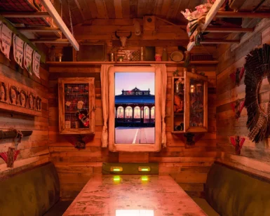 Experimenta el Escape Room Gastronómico en Madrid, con una acogedora sala de madera con decoración rústica y una ventana enmarcada con vistas a una estación de tren iluminada al atardecer, capturando el vibrante ambiente madrileño. Perfecto para quienes buscan una escapada única con un toque gastronómico. - ForTwo - Planes para parejas