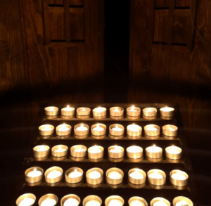 Filas de velas de té encendidas proyectan un brillo parpadeante en el interior de Escape Room La Isla de las Muñecas, mientras que los detalles de la puerta de madera en el fondo realzan su atmósfera inquietante. - ForTwo - Planes para parejas