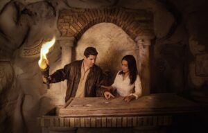 Bajo la tenue luz del goldenpop, un hombre sostiene su mano mientras una mujer examina cuidadosamente un artefacto en una losa de piedra, rodeada por la intriga de las Catacumbas de Escape Room. - ForTwo - Planes para parejas
