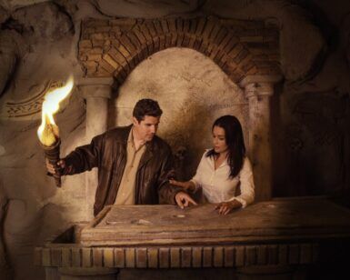 Bajo la tenue luz del goldenpop, un hombre sostiene su mano mientras una mujer examina cuidadosamente un artefacto en una losa de piedra, rodeada por la intriga de las Catacumbas de Escape Room. - ForTwo - Planes para parejas