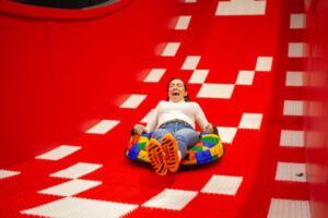 En Hi Jump Terrassa una persona disfruta de pura adrenalina y emoción mientras se desliza por un tobogán de color rojo brillante en un tubo hinchable. - ForTwo - Planes para parejas