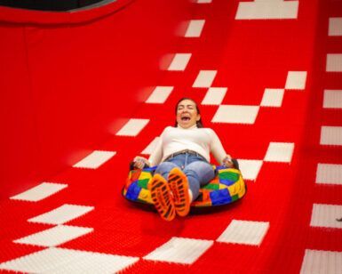 En Hi Jump Terrassa una persona disfruta de pura adrenalina y emoción mientras se desliza por un tobogán de color rojo brillante en un tubo hinchable. - ForTwo - Planes para parejas