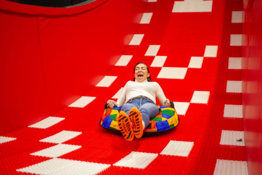 En Hi Jump Terrassa una persona disfruta de pura adrenalina y emoción mientras se desliza por un tobogán de color rojo brillante en un tubo hinchable. - ForTwo - Planes para parejas