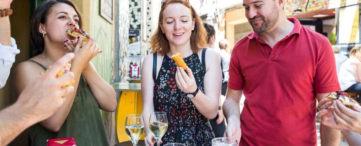 Gente disfrutando de tapas y bebidas en una mesa al aire libre en Zaragoza, sonriendo y charlando como si acabaran de visitar el Mercado de Mediodía y Tapas de Zaragoza. - ForTwo - Planes para parejas