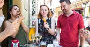 Gente disfrutando de tapas y bebidas en una mesa al aire libre en Zaragoza, sonriendo y charlando como si acabaran de visitar el Mercado de Mediodía y Tapas de Zaragoza. - ForTwo - Planes para parejas