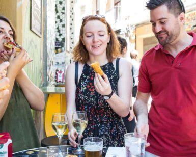 Gente disfrutando de tapas y bebidas en una mesa al aire libre en Zaragoza, sonriendo y charlando como si acabaran de visitar el Mercado de Mediodía y Tapas de Zaragoza. - ForTwo - Planes para parejas