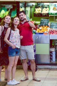 Tres personas se encuentran en el Mercado de Mediodía y Tapas en Zaragoza, rodeadas de frutas y verduras frescas, mirando hacia arriba. - ForTwo - Planes para parejas