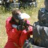 Vestido con traje y máscara de color rojo, un individuo se agacha, apuntando con su pistola de paintball cerca de unos neumáticos apilados al aire libre, listo para la acción en el emocionante terreno del Paintball en Murillo de Gállego (Zaragoza). - ForTwo - Planes para parejas