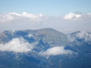 Una vista desde el "Paseo en avioneta de Zaragoza al Moncayo" captura la majestuosa sierra del Moncayo, con sus picos parcialmente ocultos por las nubes bajo un cielo azul claro. - ForTwo - Planes para parejas