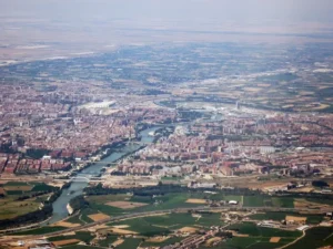 Un paseo en avión revela Zaragoza, España, donde el río Ebro serpentea con gracia entre paisajes urbanos y zonas verdes, con el imponente Moncayo en la distancia. - ForTwo - Planes para parejas