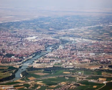 Un paseo en avión revela Zaragoza, España, donde el río Ebro serpentea con gracia entre paisajes urbanos y zonas verdes, con el imponente Moncayo en la distancia. - ForTwo - Planes para parejas