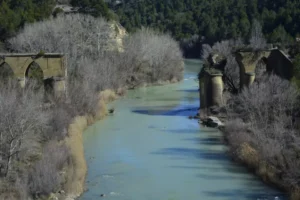 Cerca de Murillo de Gállego, un puente de piedra en ruinas cruza un río tranquilo con árboles desnudos y colinas boscosas, creando un lugar ideal para los entusiastas del Puenting en Murillo de Gállego que buscan aventura. - ForTwo - Planes para parejas