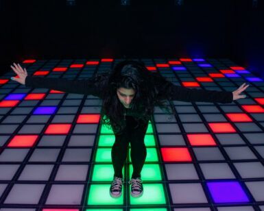 Una persona con los brazos extendidos se encuentra en una vibrante pista de baile multicolor de azul, rojo y verde. La escena evoca la vibrante experiencia de Pulse Up en Aventúrico Barcelona. - ForTwo - Planes para parejas