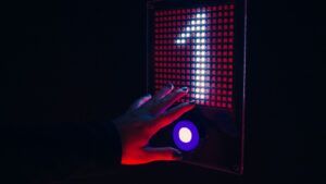 Una mano se extiende hacia un panel futurista y luminoso con un botón circular azul y una cuadrícula iluminada en rojo con una flecha blanca, que evoca la vibrante escena tecnológica de Barcelona. Descubre la experiencia: Pulse Up en Aventúrico Barcelona. - ForTwo - Planes para parejas