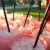 Bajo el sol de Zaragoza, vasos rosas llenos de hielo y pajitas negras están dispuestos en la mesa al aire libre, resaltando el arte del "Taller-show de coctelería en Zaragoza. - ForTwo - Planes para parejas