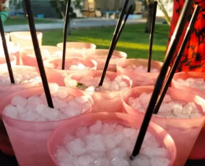 Bajo el sol de Zaragoza, vasos rosas llenos de hielo y pajitas negras están dispuestos en la mesa al aire libre, resaltando el arte del "Taller-show de coctelería en Zaragoza. - ForTwo - Planes para parejas