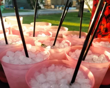Bajo el sol de Zaragoza, vasos rosas llenos de hielo y pajitas negras están dispuestos en la mesa al aire libre, resaltando el arte del "Taller-show de coctelería en Zaragoza. - ForTwo - Planes para parejas