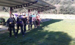 Tiro con Arco 3D en Luesia: Una Aventura en Plena Naturaleza se desarrolla al aire libre mientras los participantes se alinean bajo un dosel de metal, apuntando intensamente sus arcos a objetivos distantes. - ForTwo - Planes para parejas
