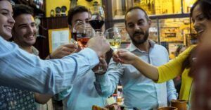 Un grupo animado choca sus copas en un brindis durante el Tour de Tapas Nocturno en Zaragoza, disfrutando del ambiente vibrante de un restaurante local. - ForTwo - Planes para parejas