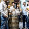 Un grupo de personas se reúne alrededor de una mesa de barril, con vasos de cerveza en mano, en una animada y decorada calle de Zaragoza. Es el escenario perfecto para su aventura del Tour de Tapas Nocturno en Zaragoza. - ForTwo - Planes para parejas