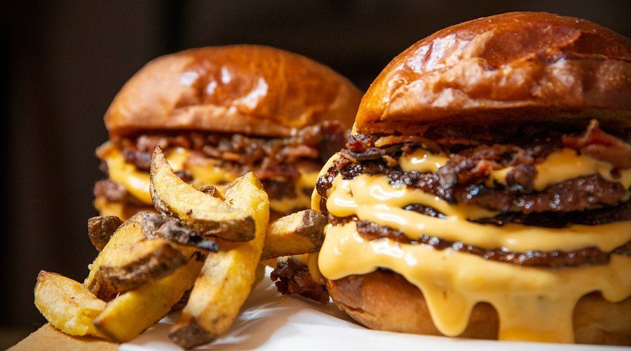 Dos hamburguesas con tocino y un acompañamiento de papas fritas sazonadas, servidas en un plato: realmente son "Dos hamburguesas: El paraíso de las hamburguesas" para los amantes de la comida reconfortante. - ForTwo - Planes para parejas
