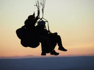 Silueta de dos personas disfrutando de un vuelo en parapente en Lucía al atardecer, con el horizonte escénico de fondo. - ForTwo - Planes para parejas