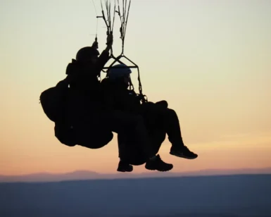 Silueta de dos personas disfrutando de un vuelo en parapente en Lucía al atardecer, con el horizonte escénico de fondo. - ForTwo - Planes para parejas