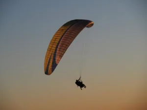 La silueta de un parapente, de "Vuelo en parapente en Luesia", se eleva con gracia al atardecer con un paracaídas vibrante recortado contra el cielo oscuro de Luesia. - ForTwo - Planes para parejas