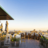 B-Heaven Rooftop Barcelona ofrece una experiencia elegante con sillas, mesas y grandes letras iluminadas que forman la palabra VIEW, todo ello perfectamente ambientado con un impresionante paisaje urbano al atardecer. - ForTwo - Planes para parejas
