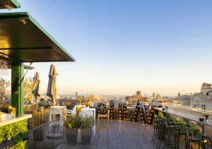 B-Heaven Rooftop Barcelona ofrece una experiencia elegante con sillas, mesas y grandes letras iluminadas que forman la palabra VIEW, todo ello perfectamente ambientado con un impresionante paisaje urbano al atardecer. - ForTwo - Planes para parejas