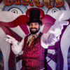 Un extraño artista de circo con chaleco y sombrero de copa se sitúa delante de un fondo con una cara de payaso con la palabra "CIRCUS" claramente encima, invitándote a vivir la experiencia Bizarre Escape Room Barcelona. - ForTwo - Planes para parejas
