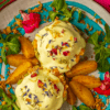 El "Brunch más original en Barcelona" está bellamente ambientado con un vibrante fondo rosa, presentando un llamativo plato de huevos Benedict adornado con flores comestibles y patatas. - ForTwo - Planes para parejas