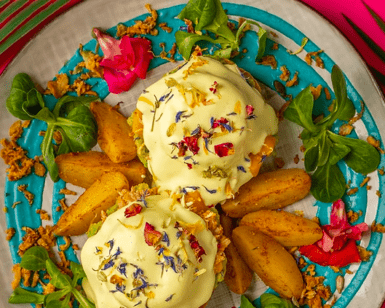 El "Brunch más original en Barcelona" está bellamente ambientado con un vibrante fondo rosa, presentando un llamativo plato de huevos Benedict adornado con flores comestibles y patatas. - ForTwo - Planes para parejas